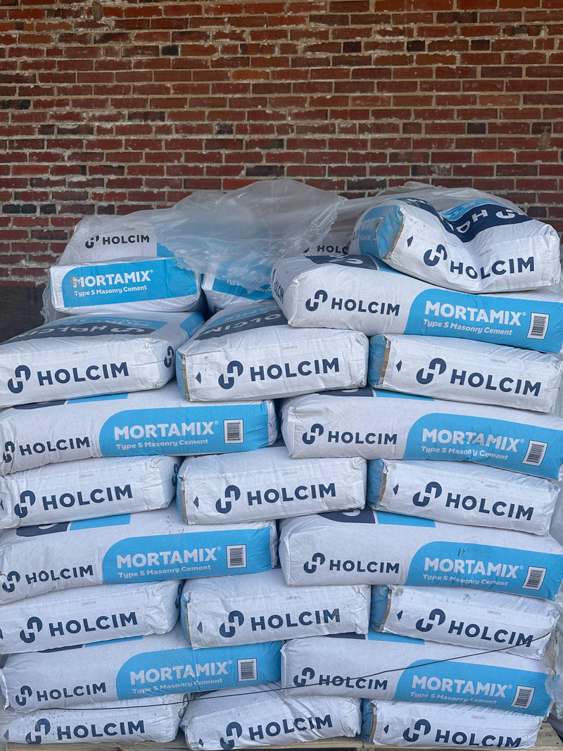 Bags of Holcim Mortamix Type S Masonry Cement stacked on a pallet in front of a brick wall, with remnants of plastic wrap visible.